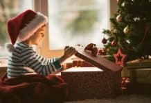 Leuchtende Kinderaugen unterm Weihnachtsbaum Little boy opening Christmas present, smiling and looking at shiny box.