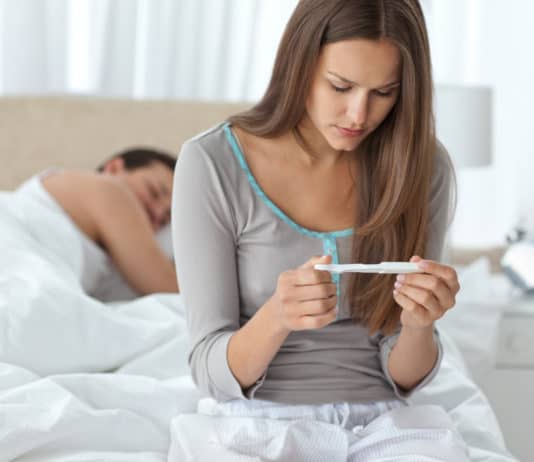 What It Feels Like to Want Children: Ten Real-Life Stories Pretty woman looking a pregnancy test while her boyfriend sleepi