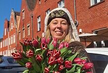 Blumenstrauß mit roten Tulpen, gehalten von einer lachenden Frau vor roten Backsteinhäusern.