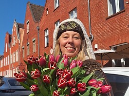 Tulpenfest läutet Frühling in Potsdam ein Blumenstrauß mit roten Tulpen, gehalten von einer lachenden Frau vor roten Backsteinhäusern.